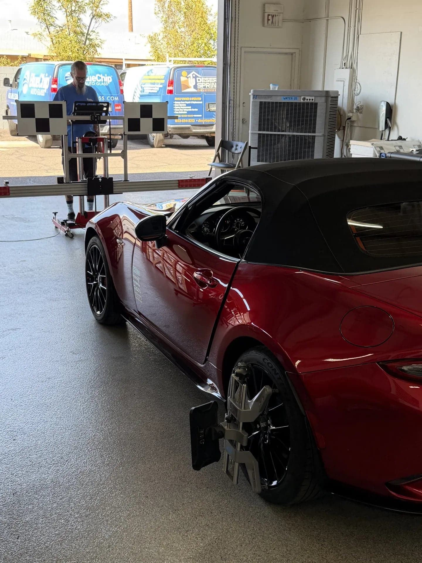 Optical positioning target clamped to the rear wheel of a red Mazda Miata, with the calibration frame ahead