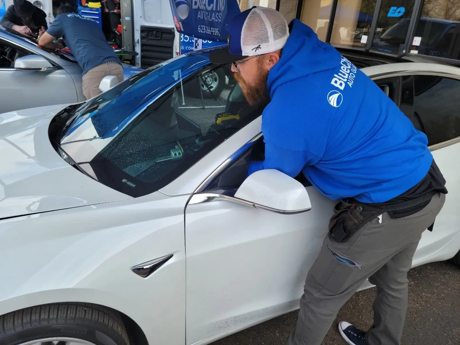 Blue Chip technician fitting a windshield on a white Tesla
