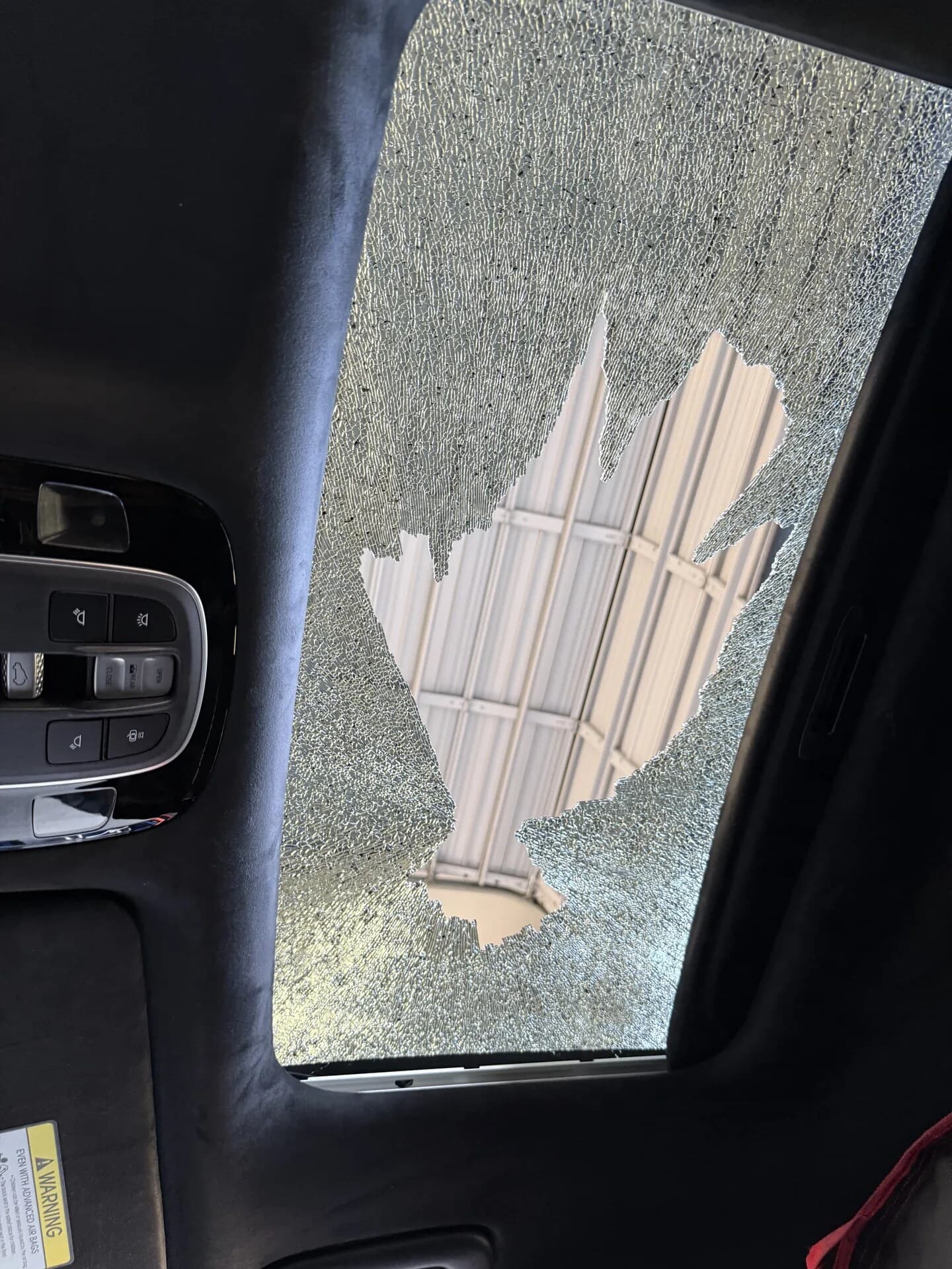 Shattered tempered sunroof glass, broken into thousands of small pieces with a hole through the middle, seen from inside the car