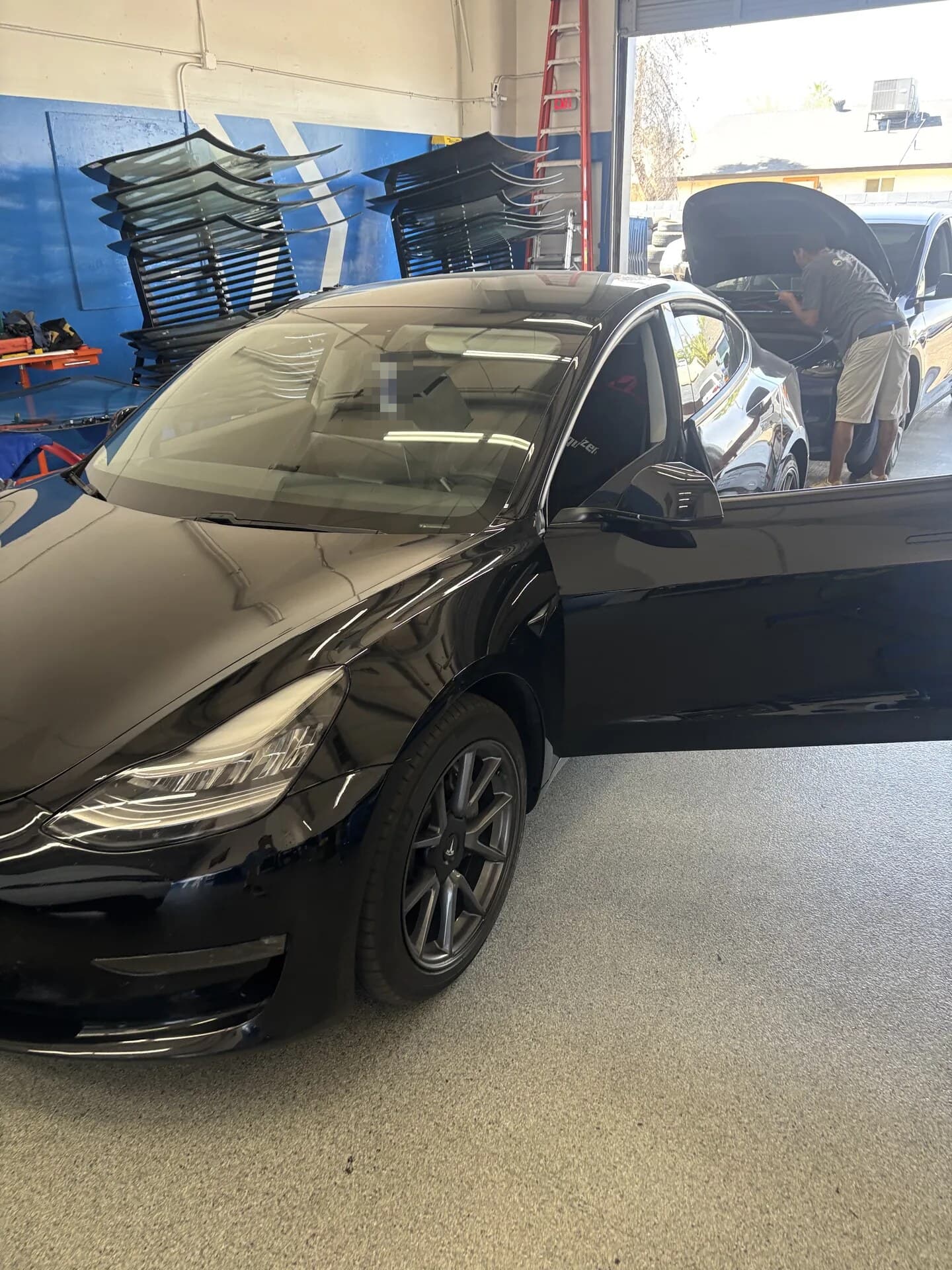 Black Tesla Model 3 with the driver door open in the Blue Chip Auto Glass shop