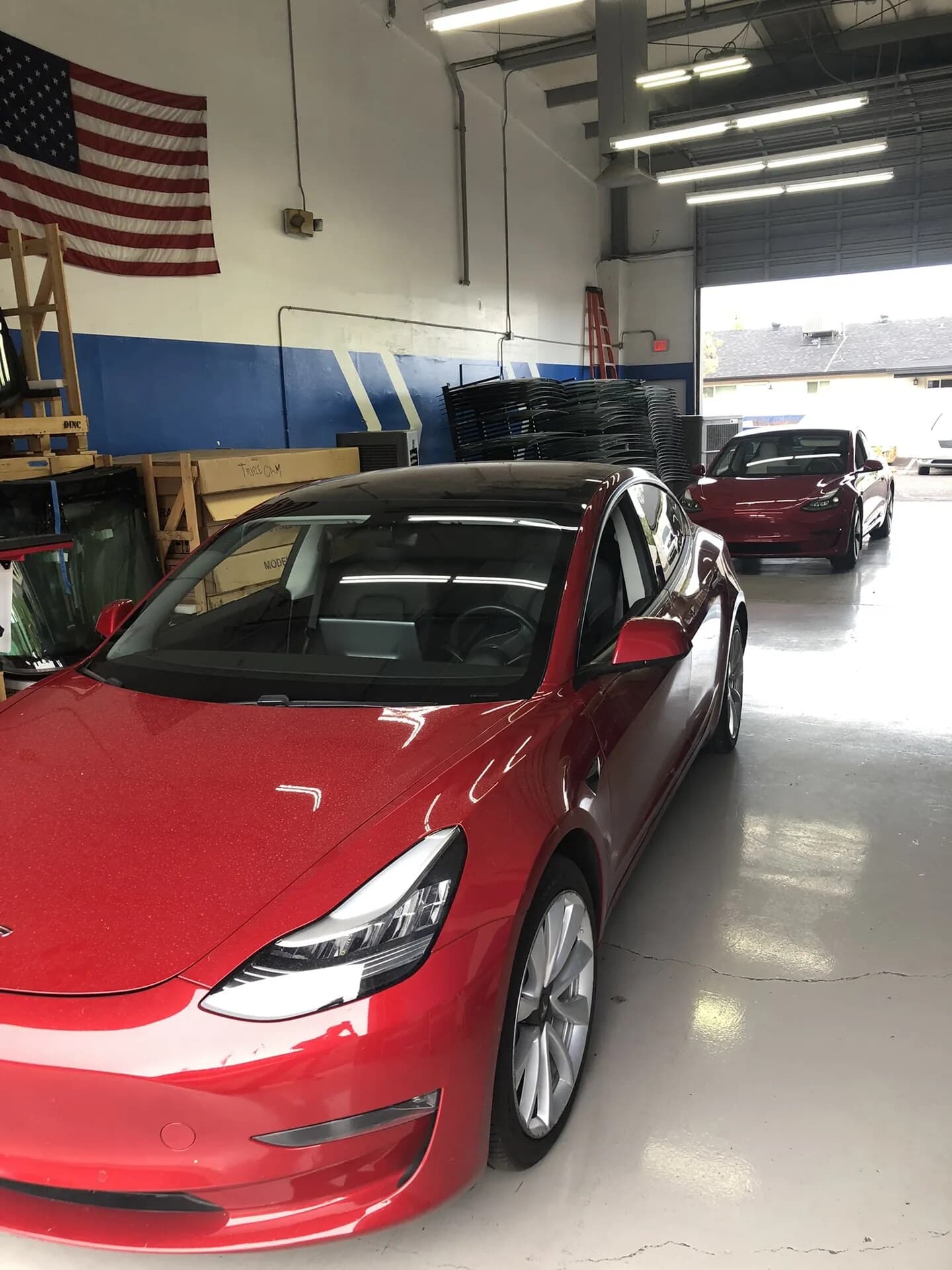 Red Tesla Model 3 in the Blue Chip Auto Glass shop with another Model 3 behind it