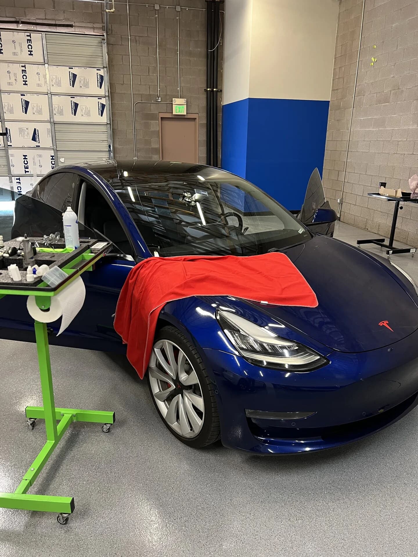 Blue Tesla Model 3 in the Blue Chip Auto Glass shop with a windshield repair tool set up on the glass