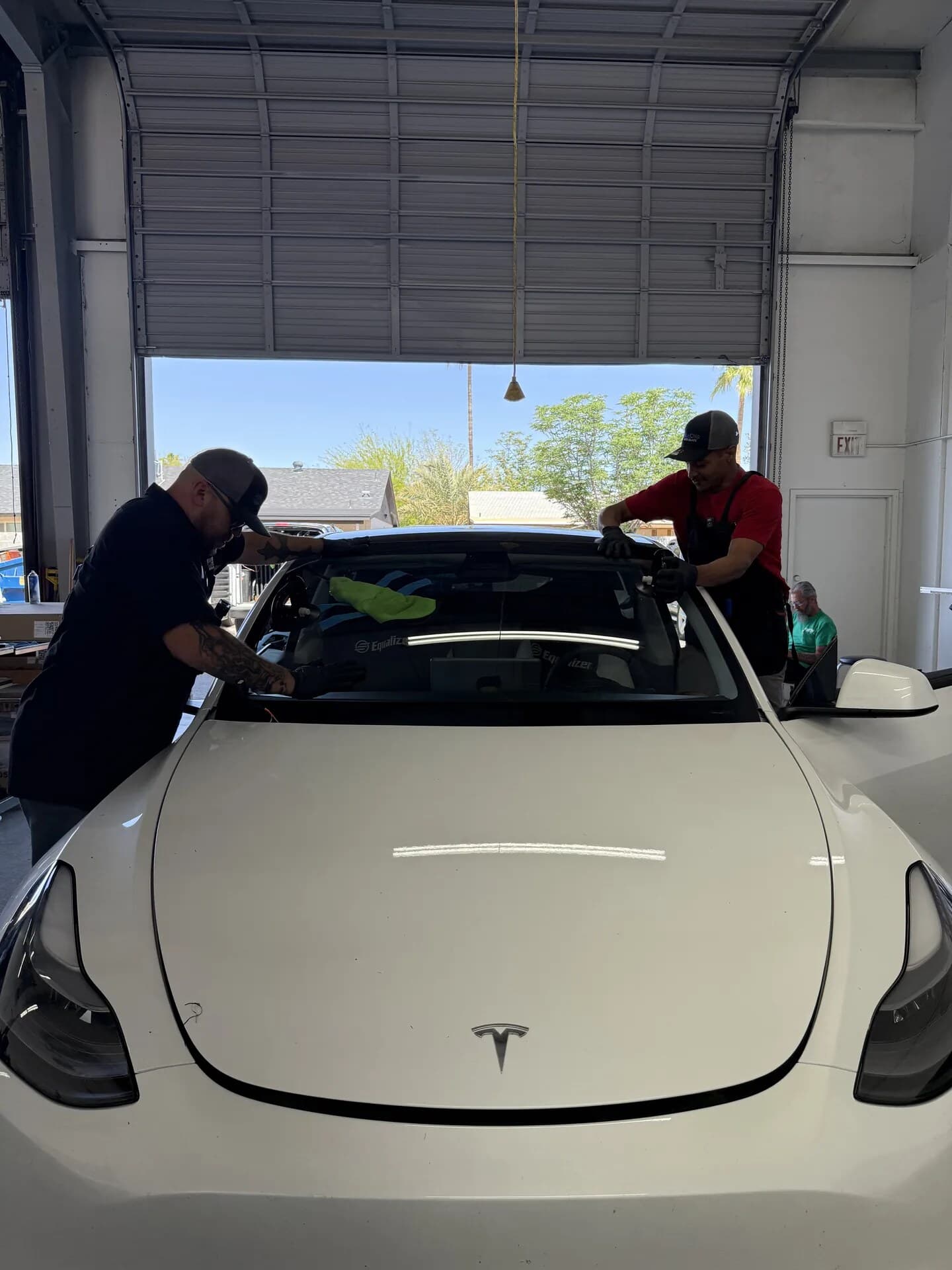 Two Blue Chip technicians setting a new windshield on a white Tesla Model 3 with suction cups