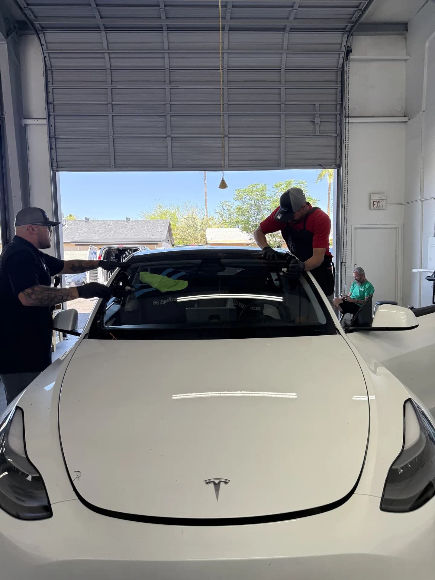 Two Blue Chip technicians setting a new windshield on a white Tesla Model 3 in the shop