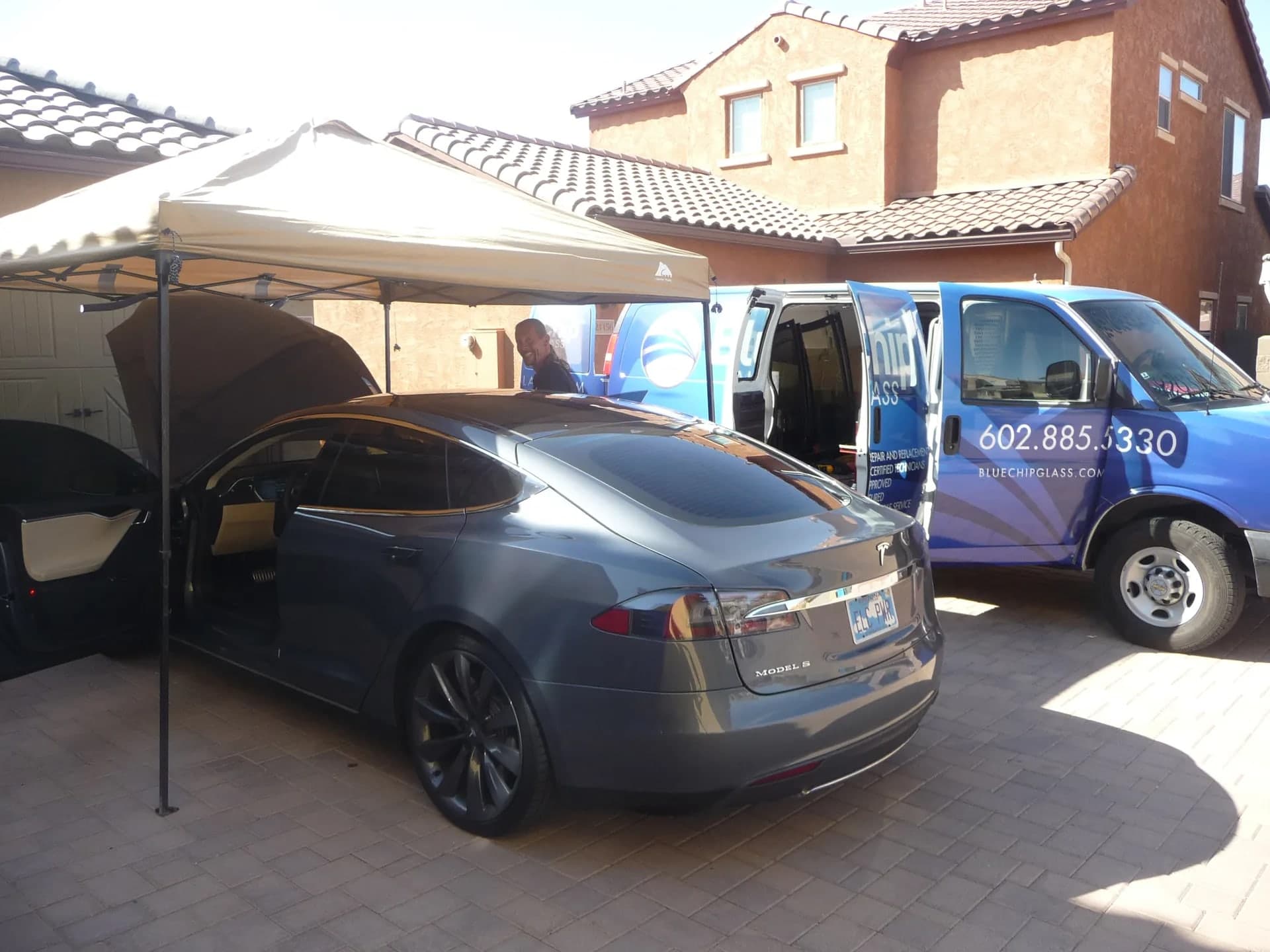 Blue Chip technicians replacing a Tesla Model S windshield under a canopy at a customer's home