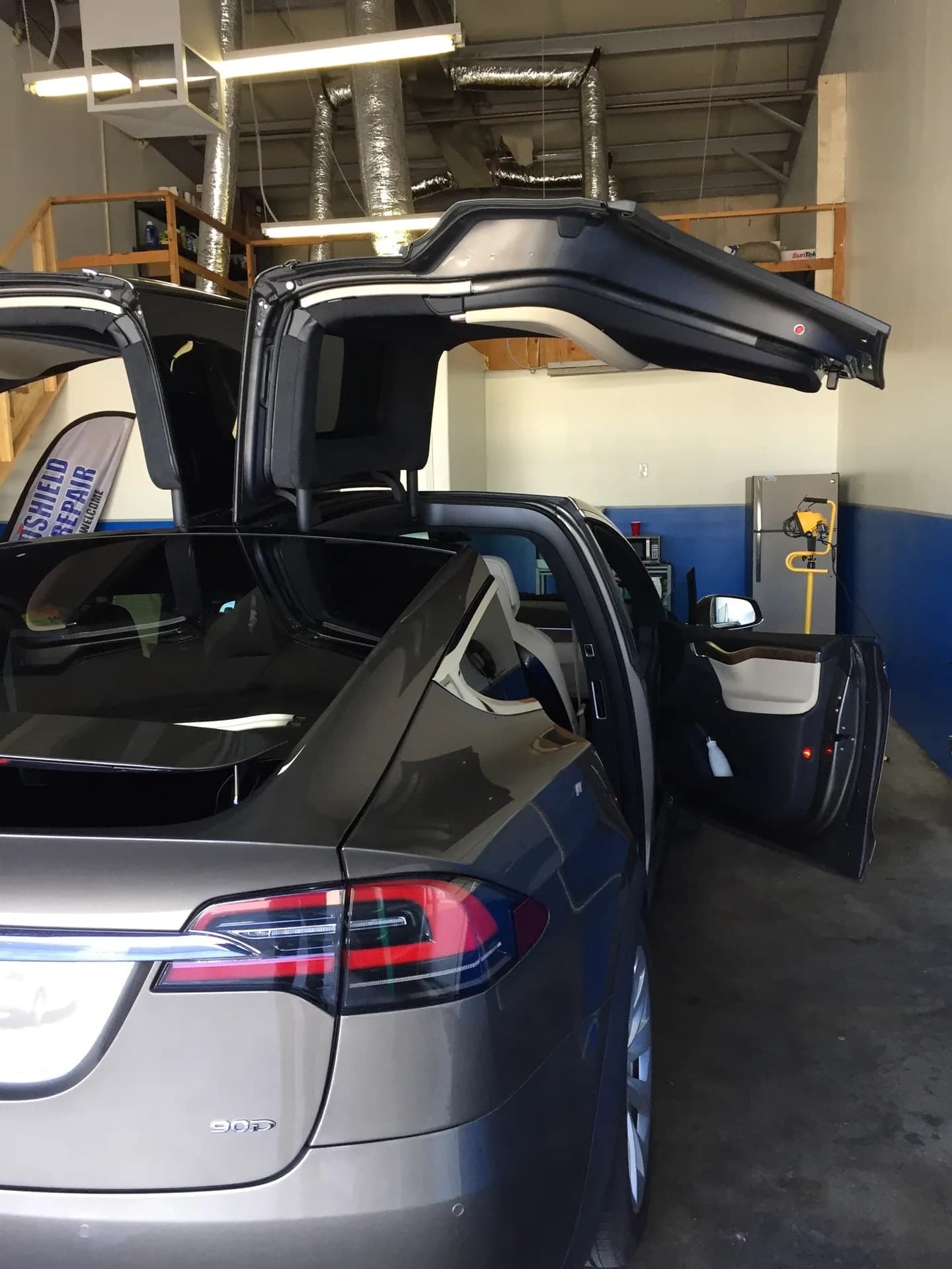 Tesla Model X with its Falcon Wing doors open in the Blue Chip Auto Glass shop