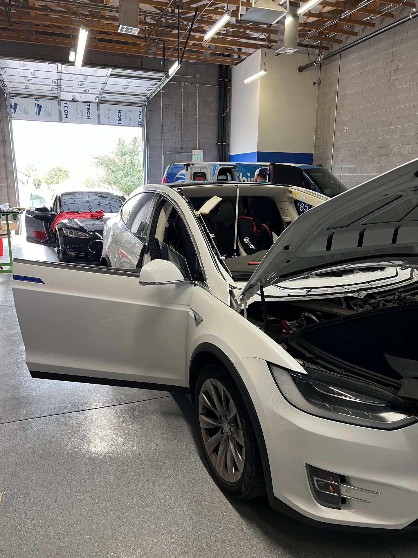 White Tesla Model X with the windshield out and the frunk open in the Blue Chip Auto Glass shop