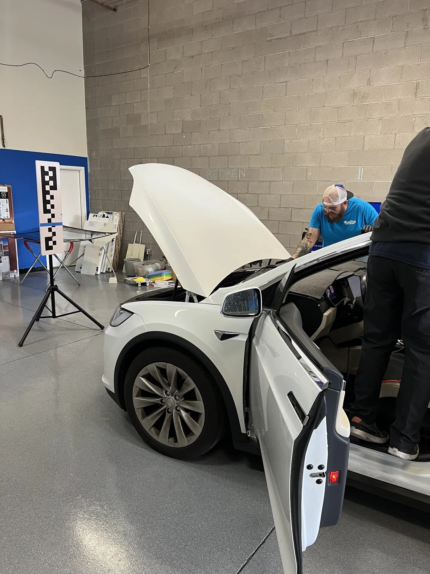 Blue Chip technicians working on a Tesla Model X with the camera calibration target set up beside it