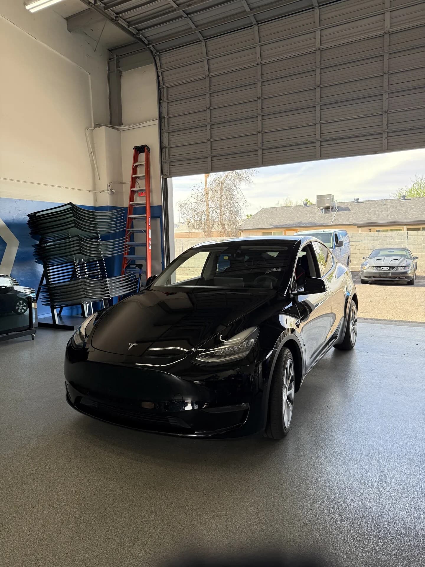 Black Tesla Model Y in the Blue Chip Auto Glass shop with Tesla windshields racked behind it