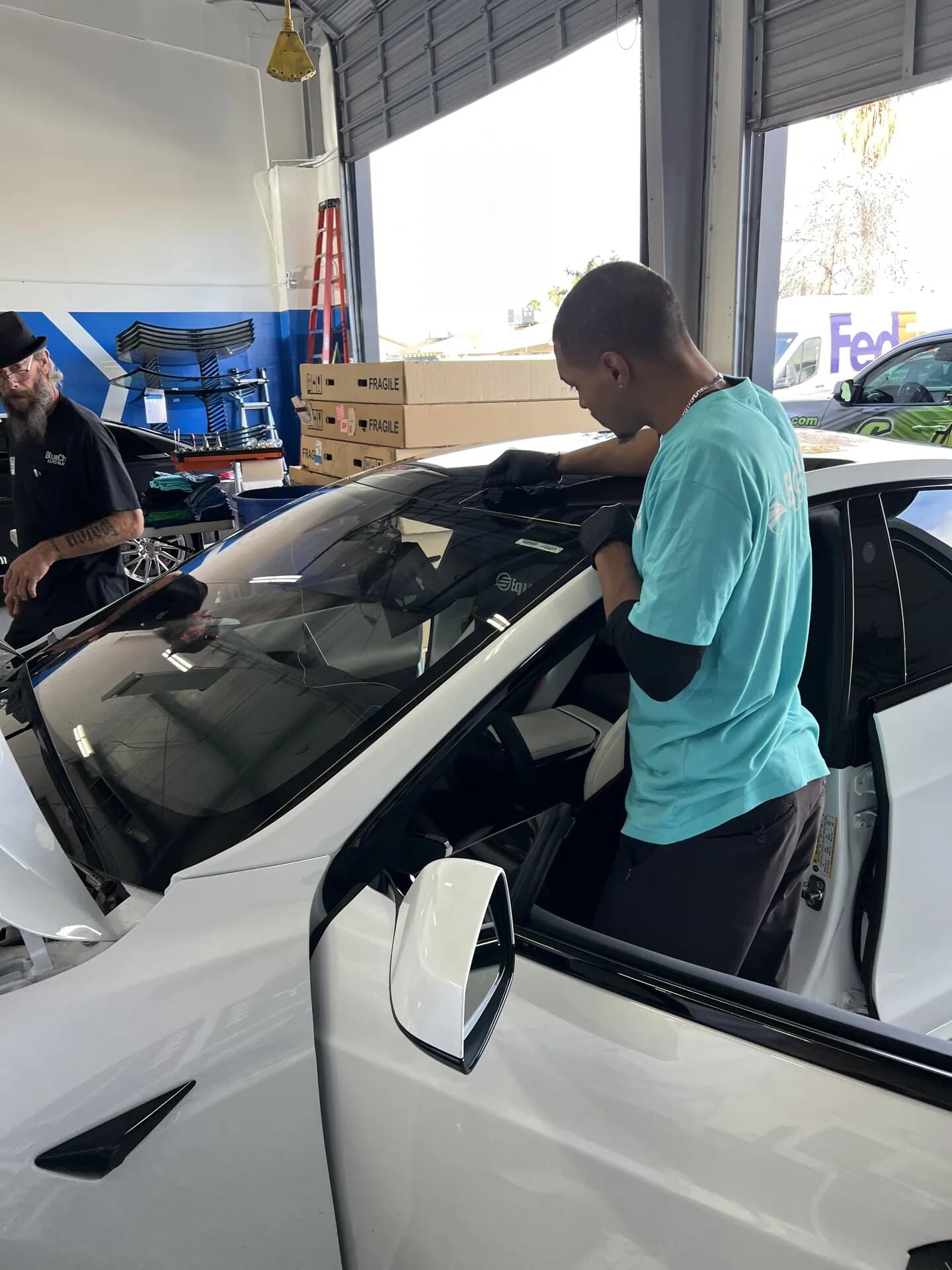 Two Blue Chip technicians setting a new windshield on a white Tesla in the shop