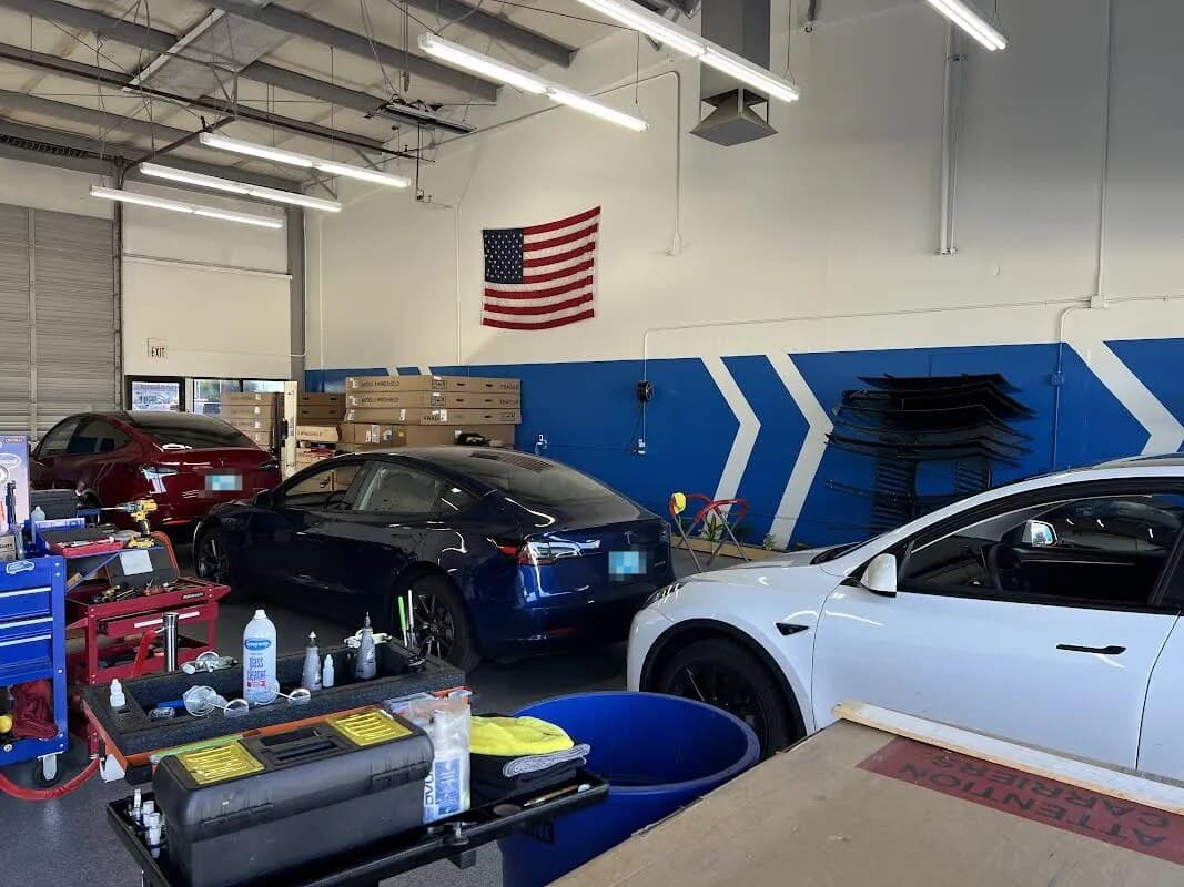Tesla Model 3s and a Model Y in the Blue Chip Auto Glass Phoenix shop, with Model Y windshields boxed and racked by the blue wall