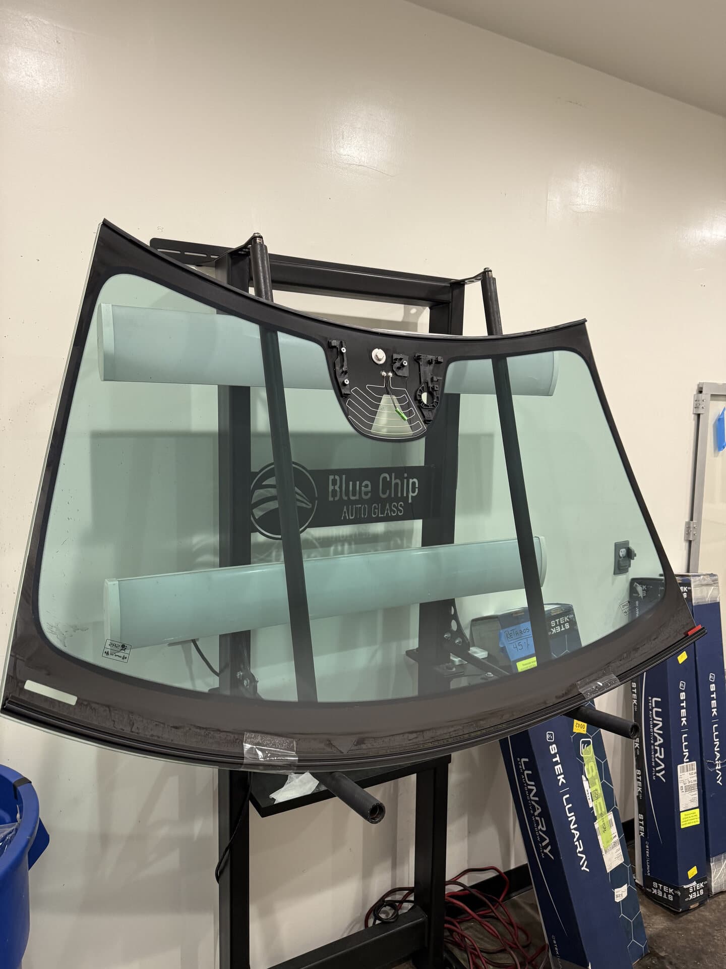 Replacement windshield on a stand in the Blue Chip Auto Glass tint room, ready for film before installation